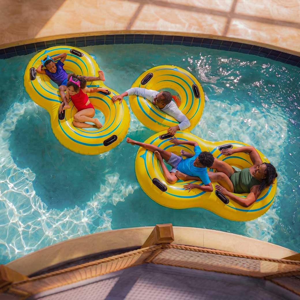 Aerial view of people relaxing on interconnected yellow inflatable tubes in a pool, enjoying a sunny day.