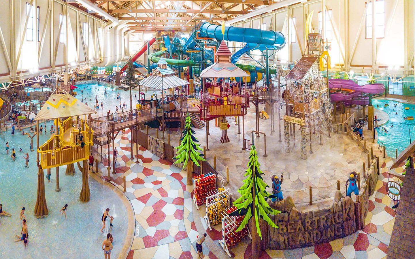 Indoor water park featuring colorful slides, splash zones, a wave pool, and play structures with families and children enjoying the attractions.