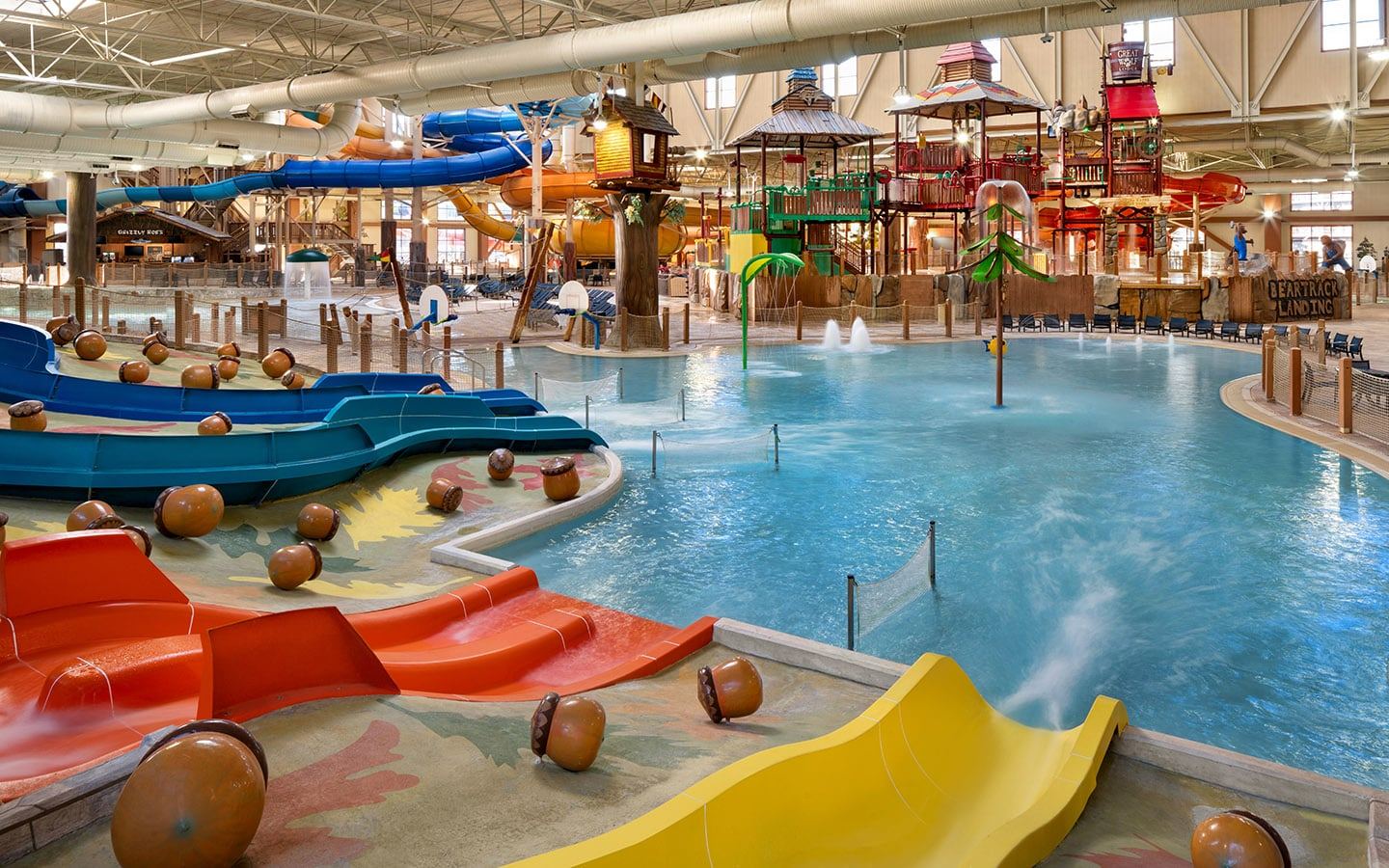 Indoor water park with colorful slides, splash pools, and playful structures. Brightly lit space with large, interconnected water play areas.