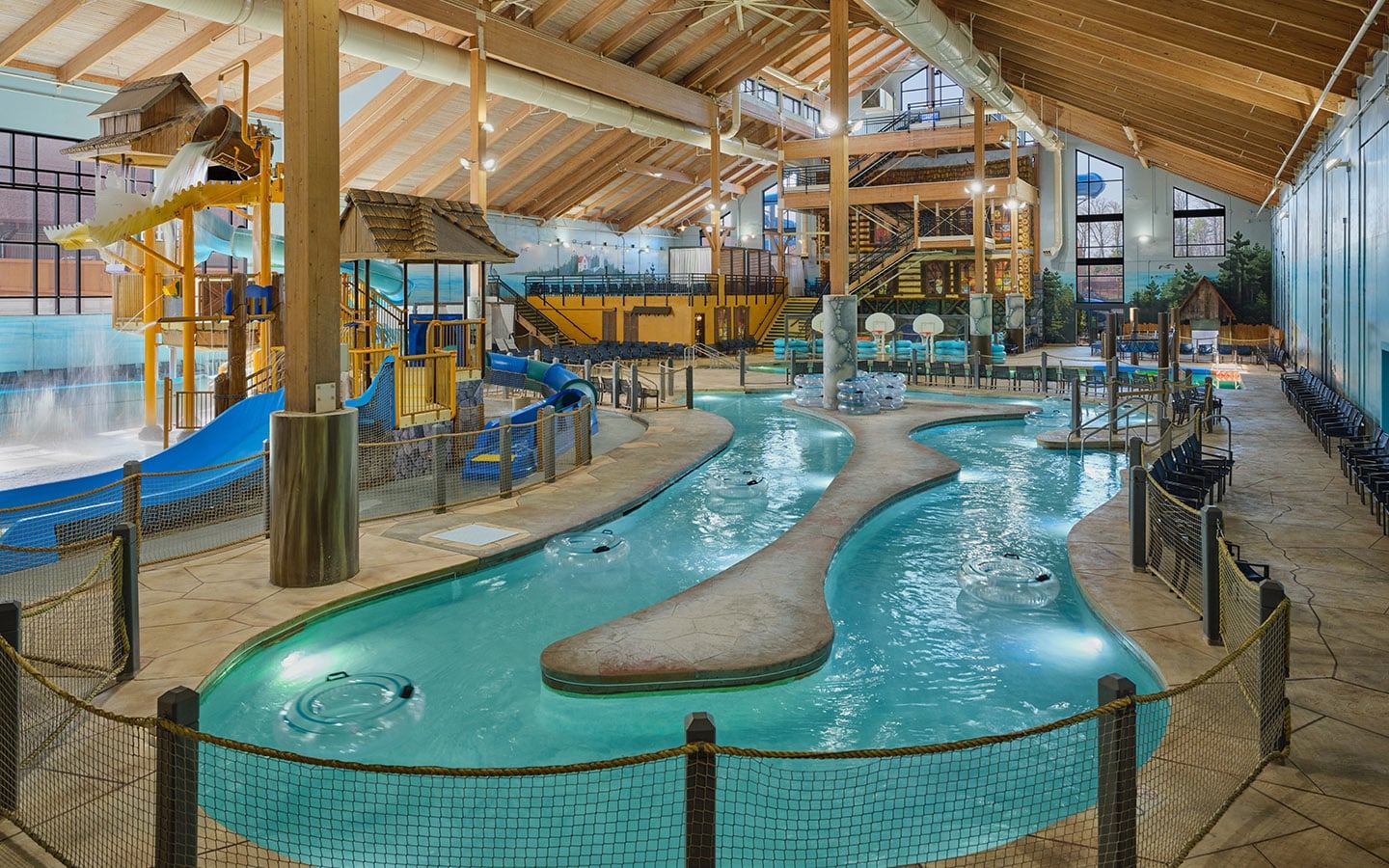 Indoor water park with slides, a lazy river, and seating areas. The structure features wooden beams and bright, child-friendly decor.