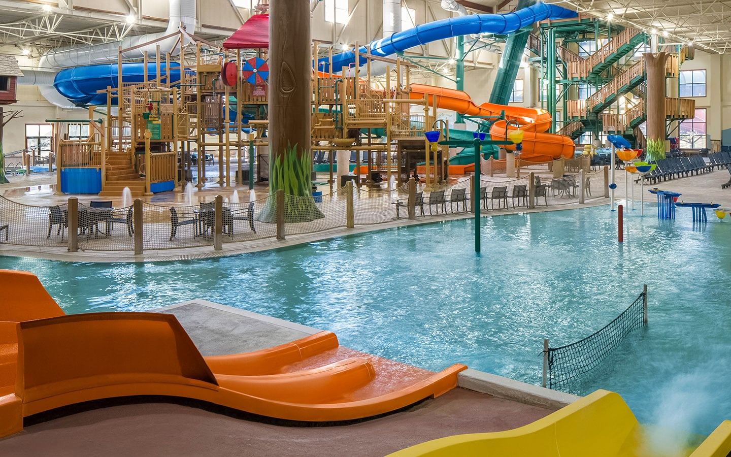 Indoor water park featuring colorful slides, structures, and a pool with lounge chairs surrounding the area under a high ceiling.