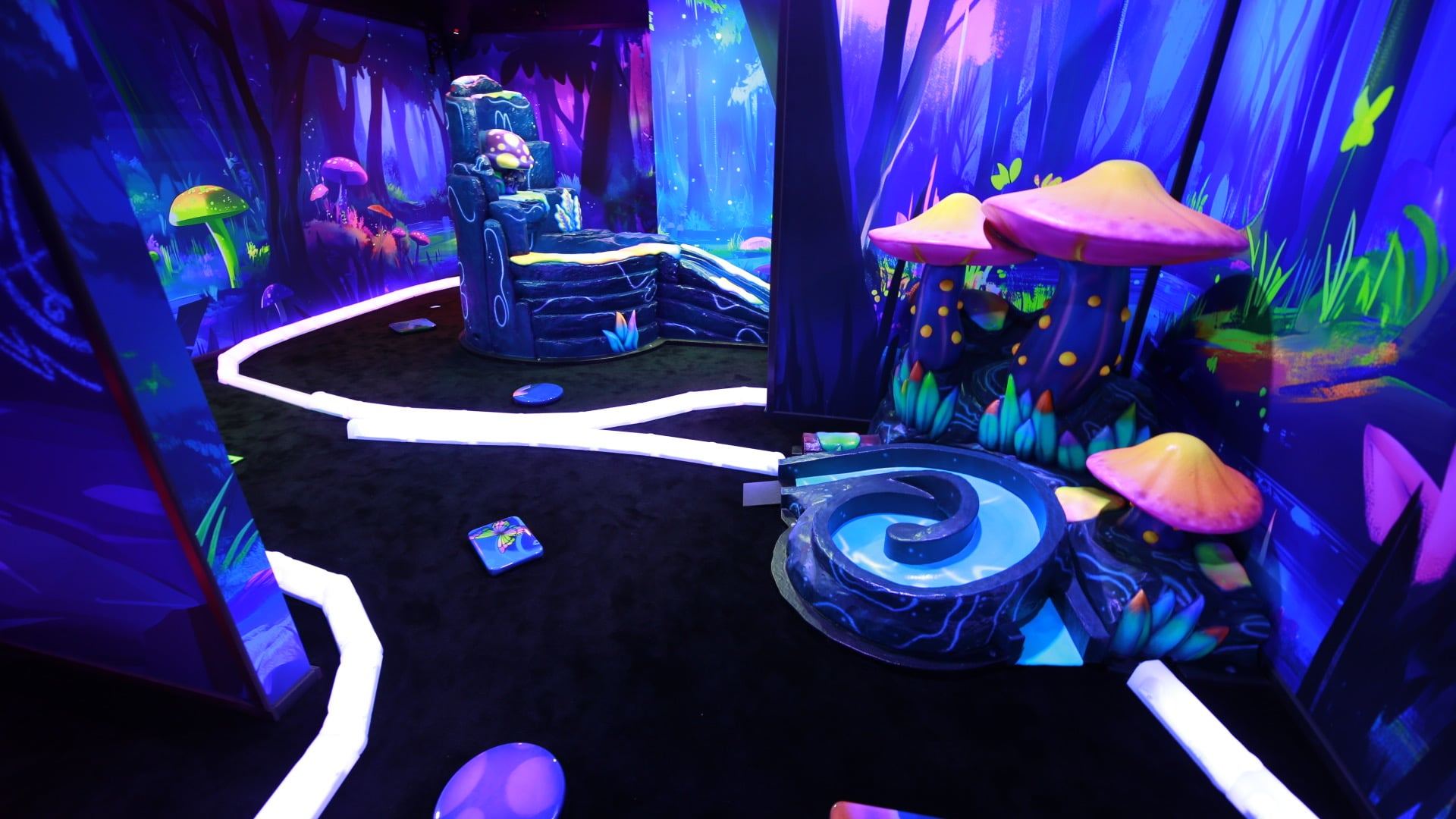 Glowing mini-golf course with vibrant, fantasy-themed decor featuring neon mushrooms, lush backdrops, and a spiral water hazard under blacklight.