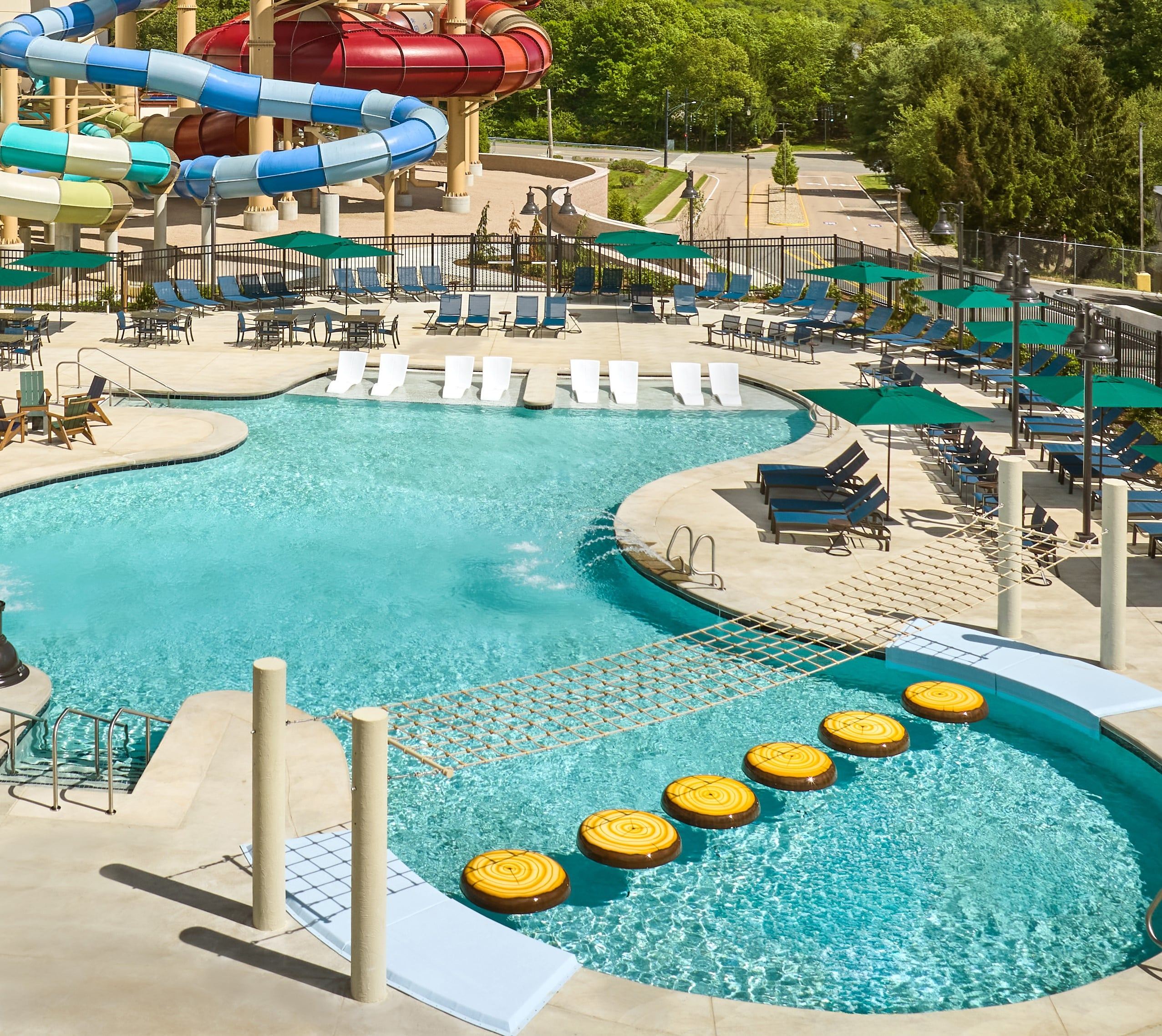 Outdoor water park with curved pool, colorful tube slides, lounge chairs, and playful stepping stones.