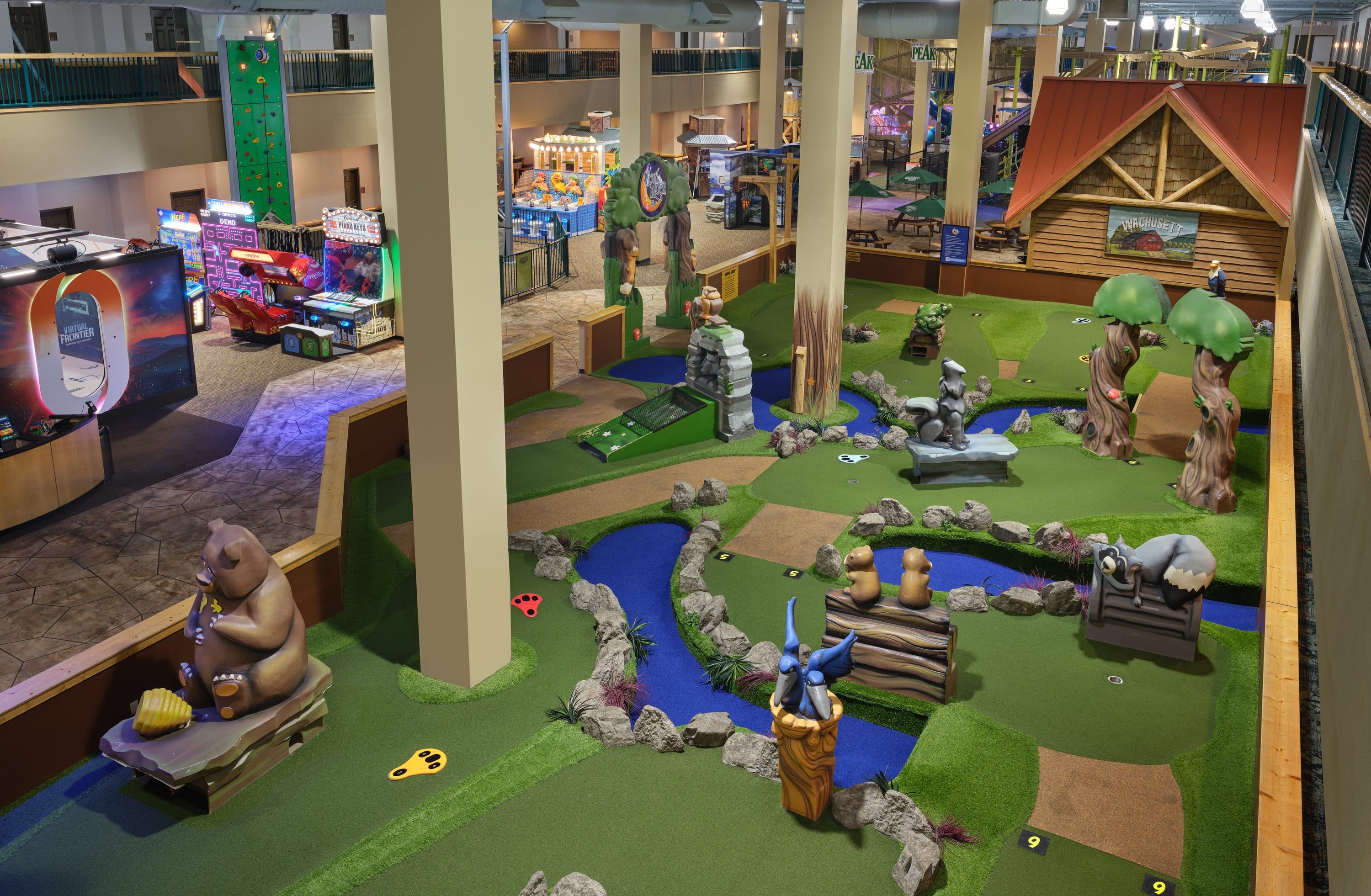Indoor mini-golf course with animal sculptures and vibrant features, adjacent to an arcade with various colorful games and a climbing structure.
