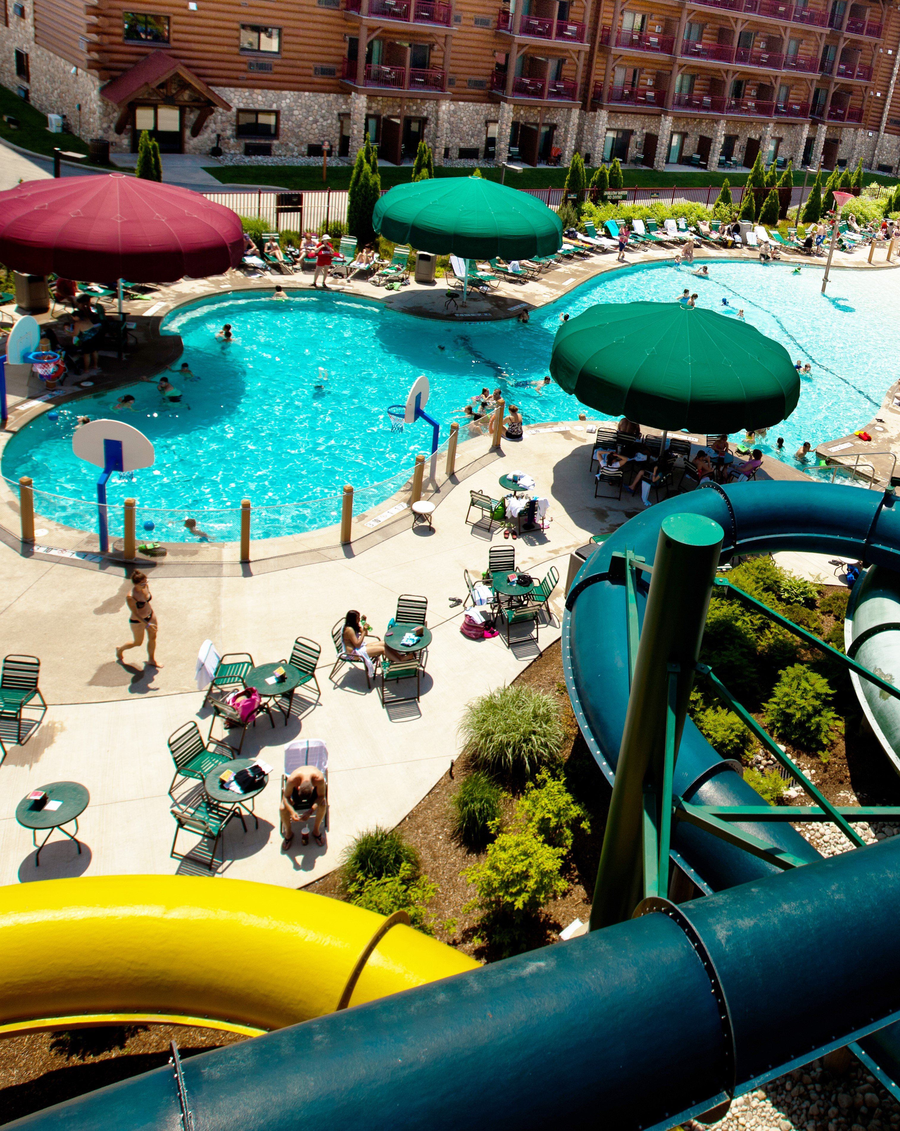 Outdoor water park with a swimming pool, waterslides, lounge chairs, and large sun umbrellas.