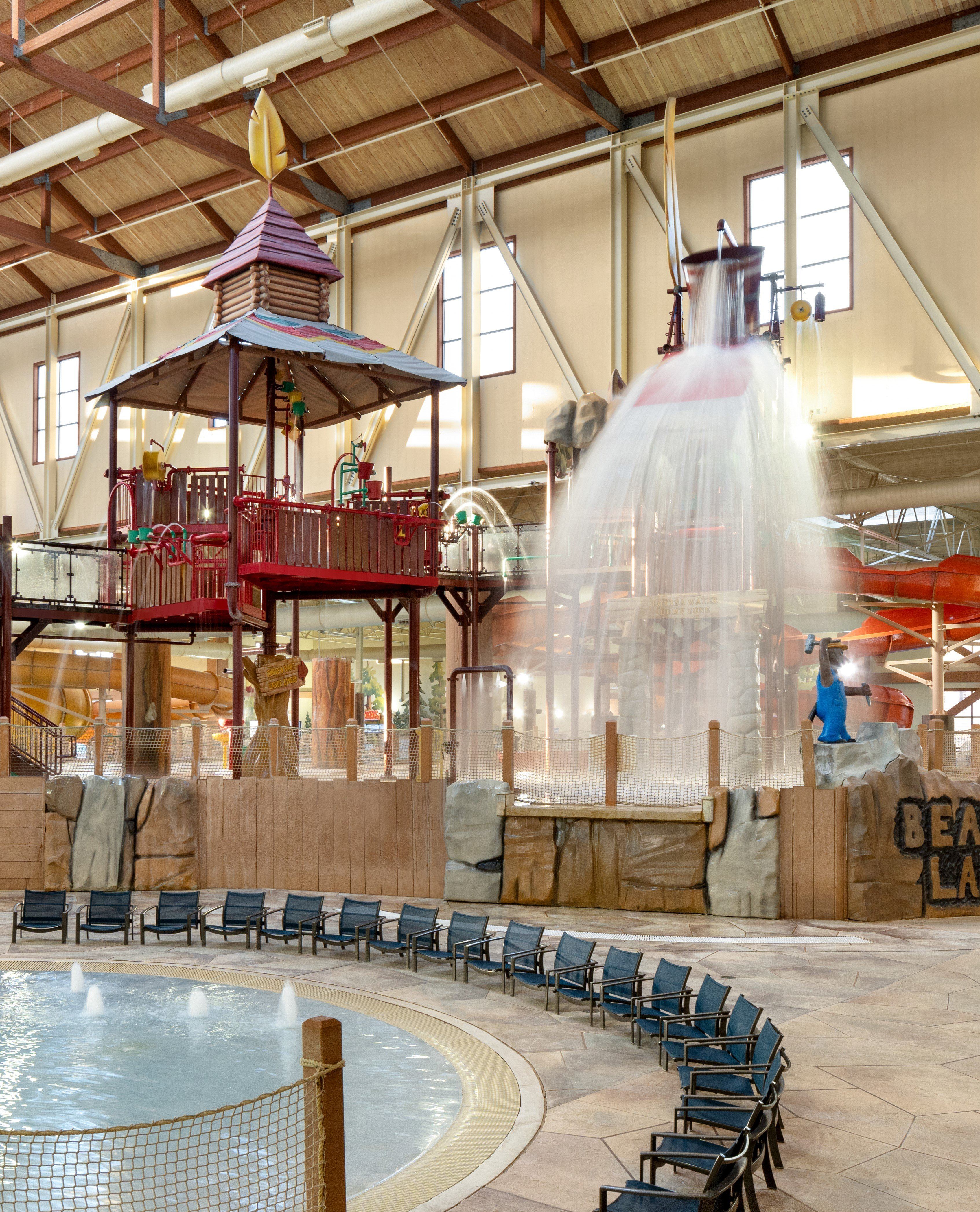 Indoor water park with a large play structure, water slides, and empty lounge chairs surrounding a shallow pool.
