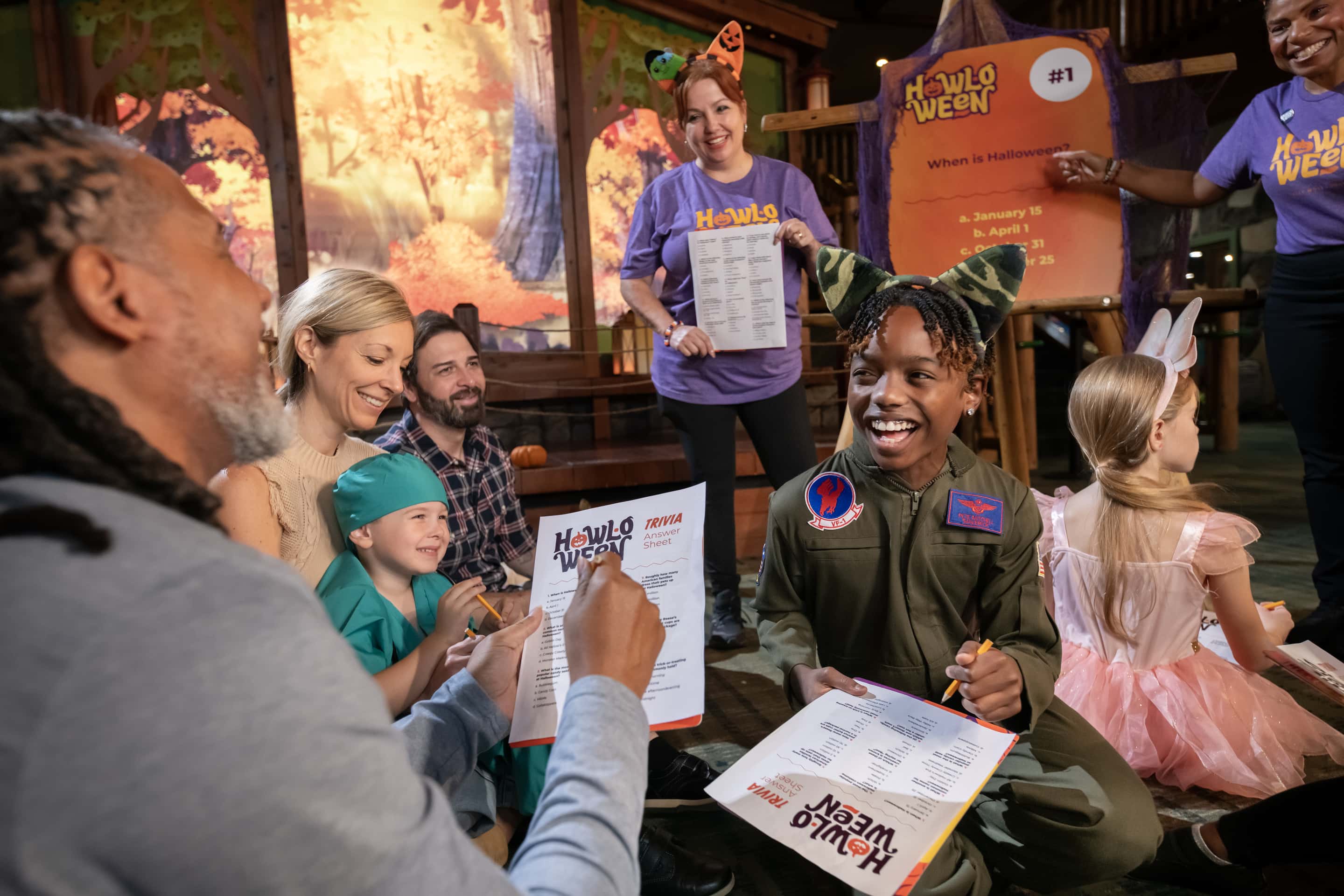 Families in Halloween costumes laugh while playing Howl-O-Ween trivia with Great Wolf Lodge staff.