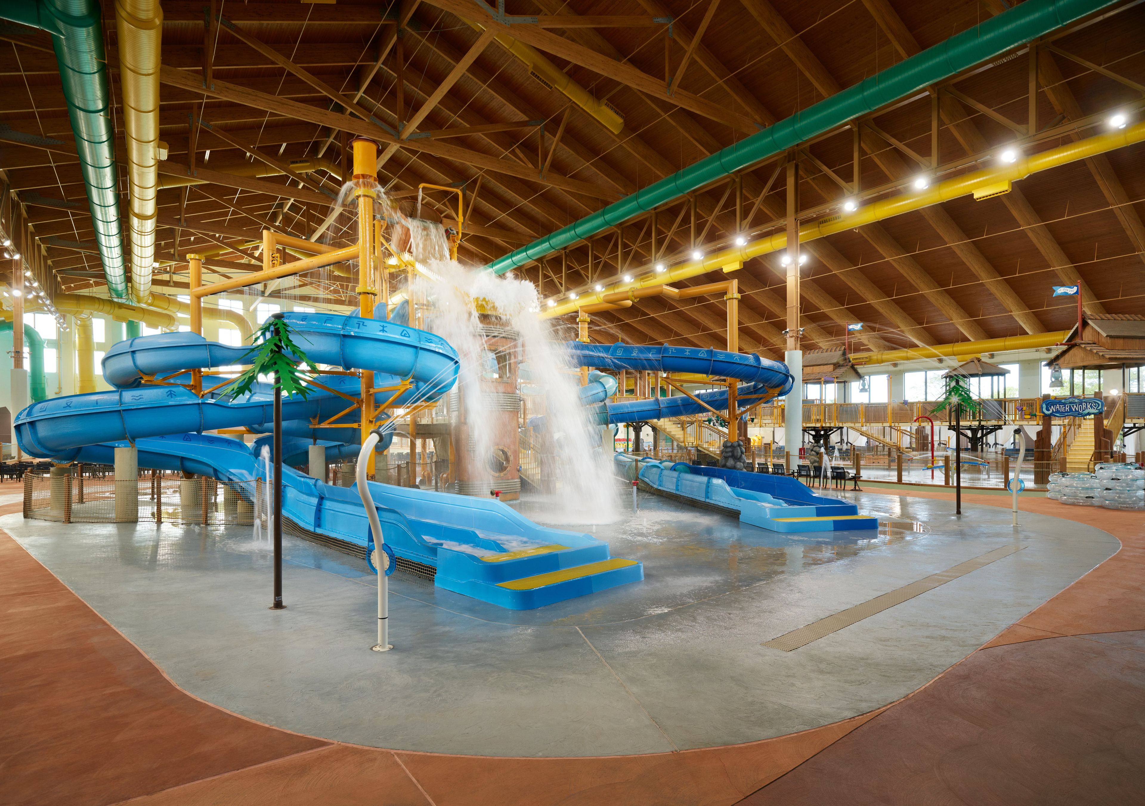 Indoor water park with blue slides, cascading waterfalls, and a high wooden ceiling, creating a vibrant and fun aquatic environment.