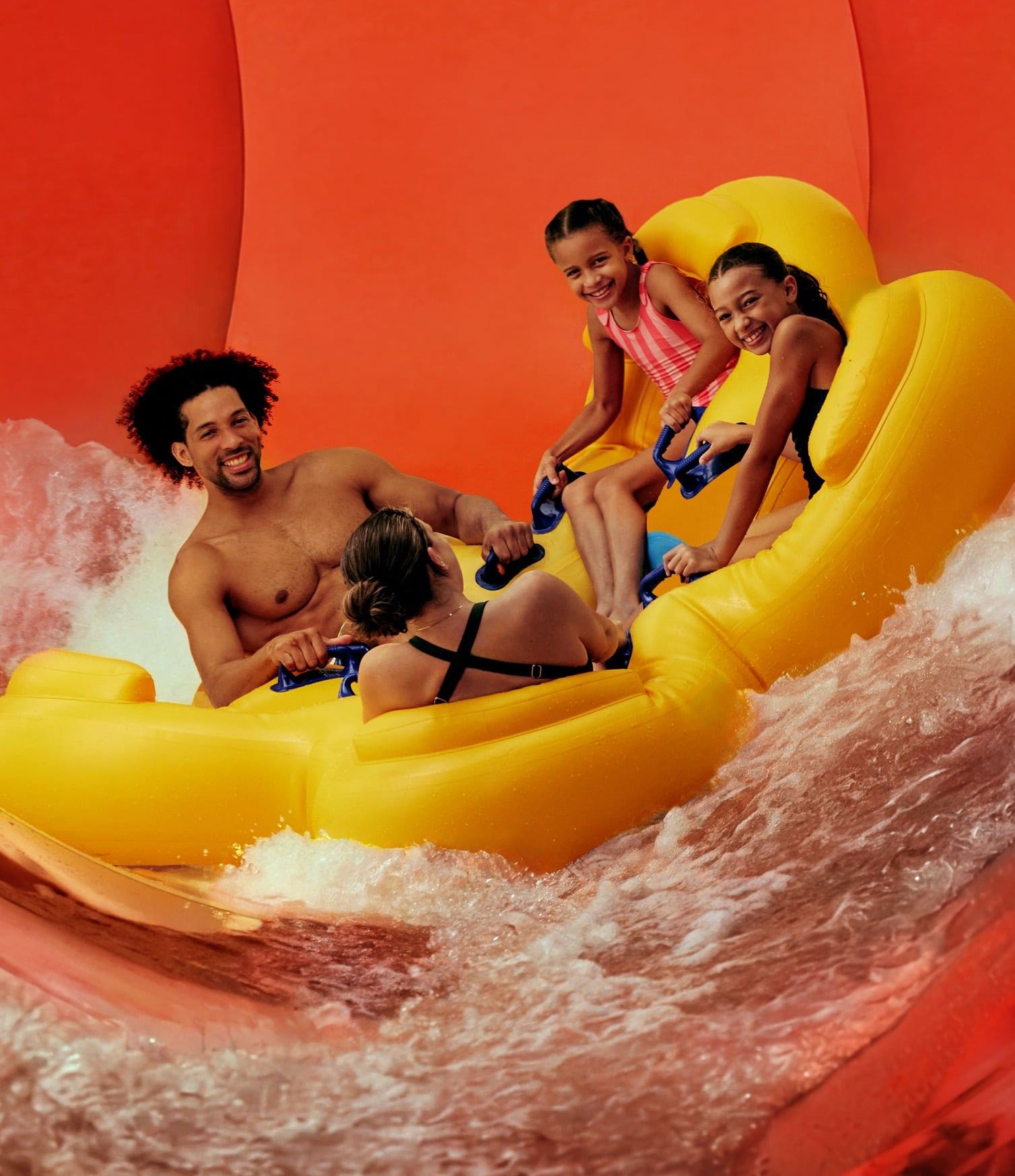 A group of four people enjoys a thrilling ride on a yellow inflatable raft inside a large, twisting red water slide.