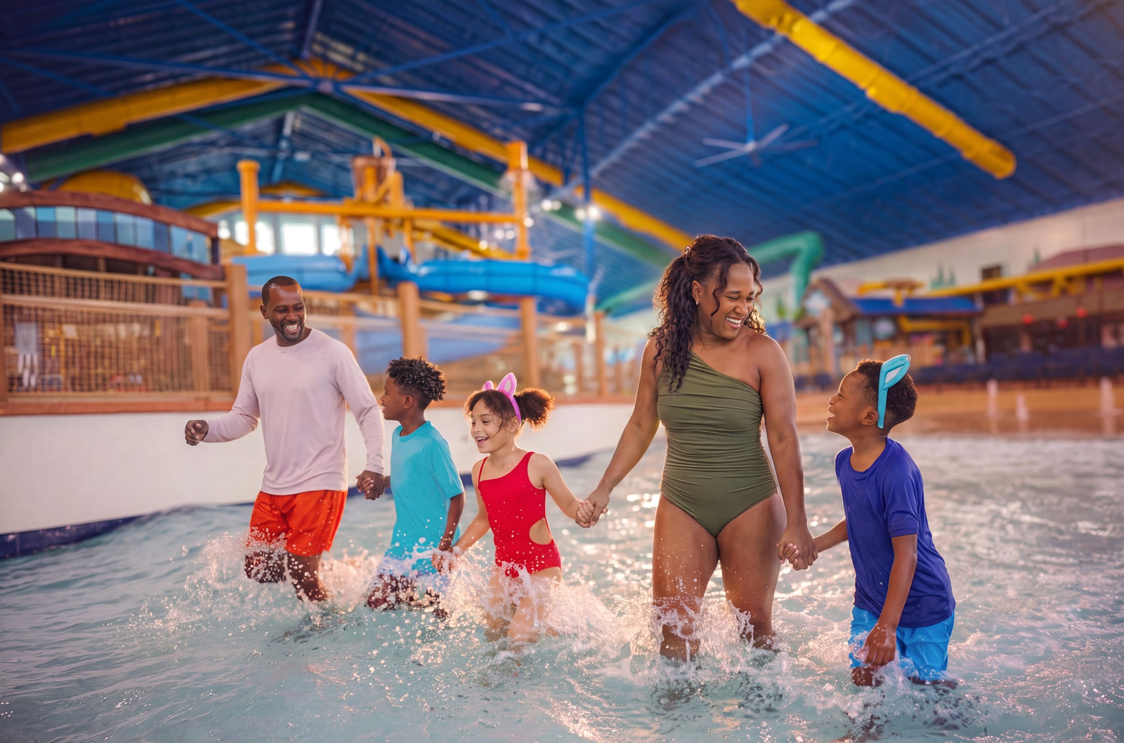 A family of five joyfully walks through shallow water in an indoor water park, surrounded by colorful water slides and structures.