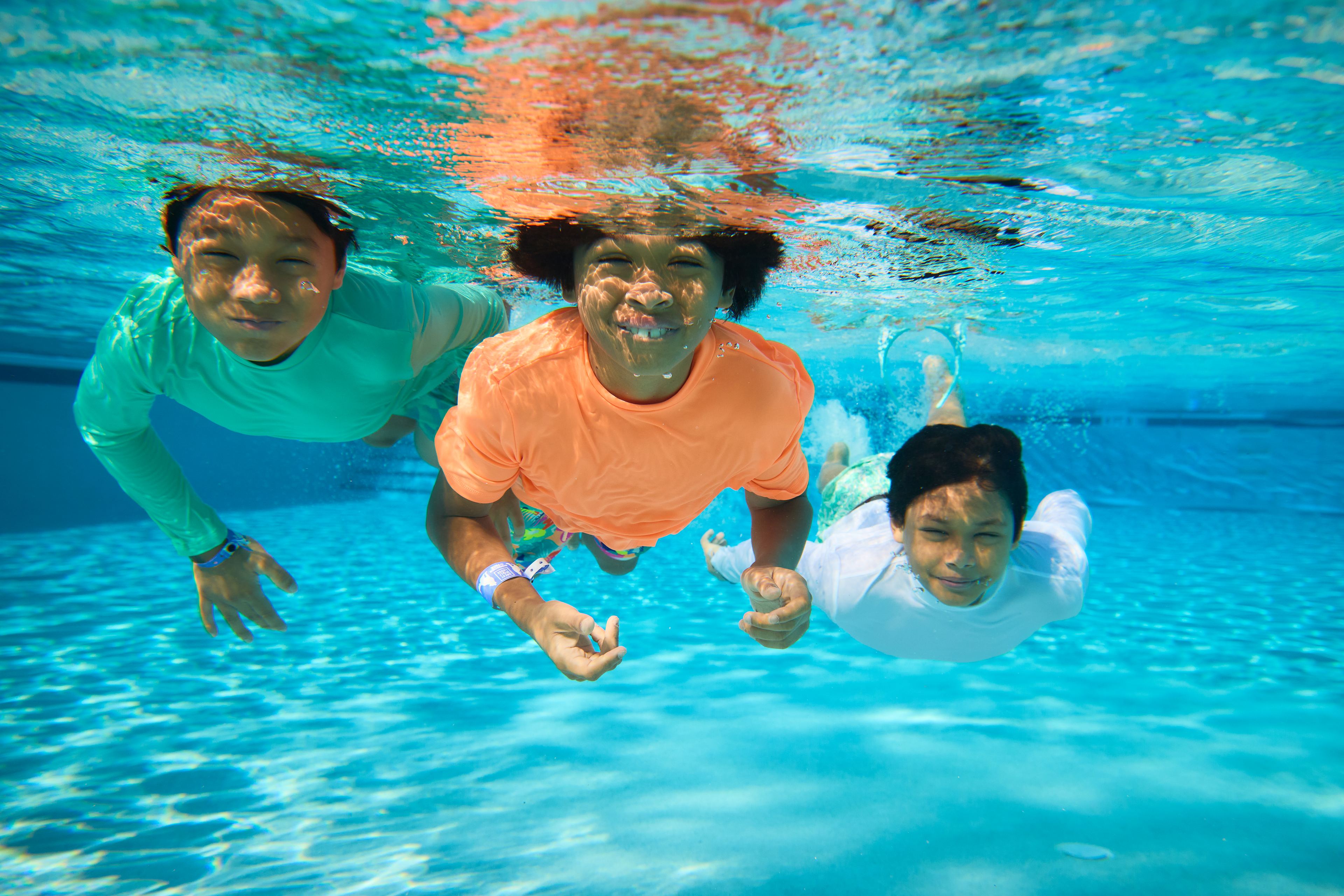 three kids in a swimming pool smiling at the camera