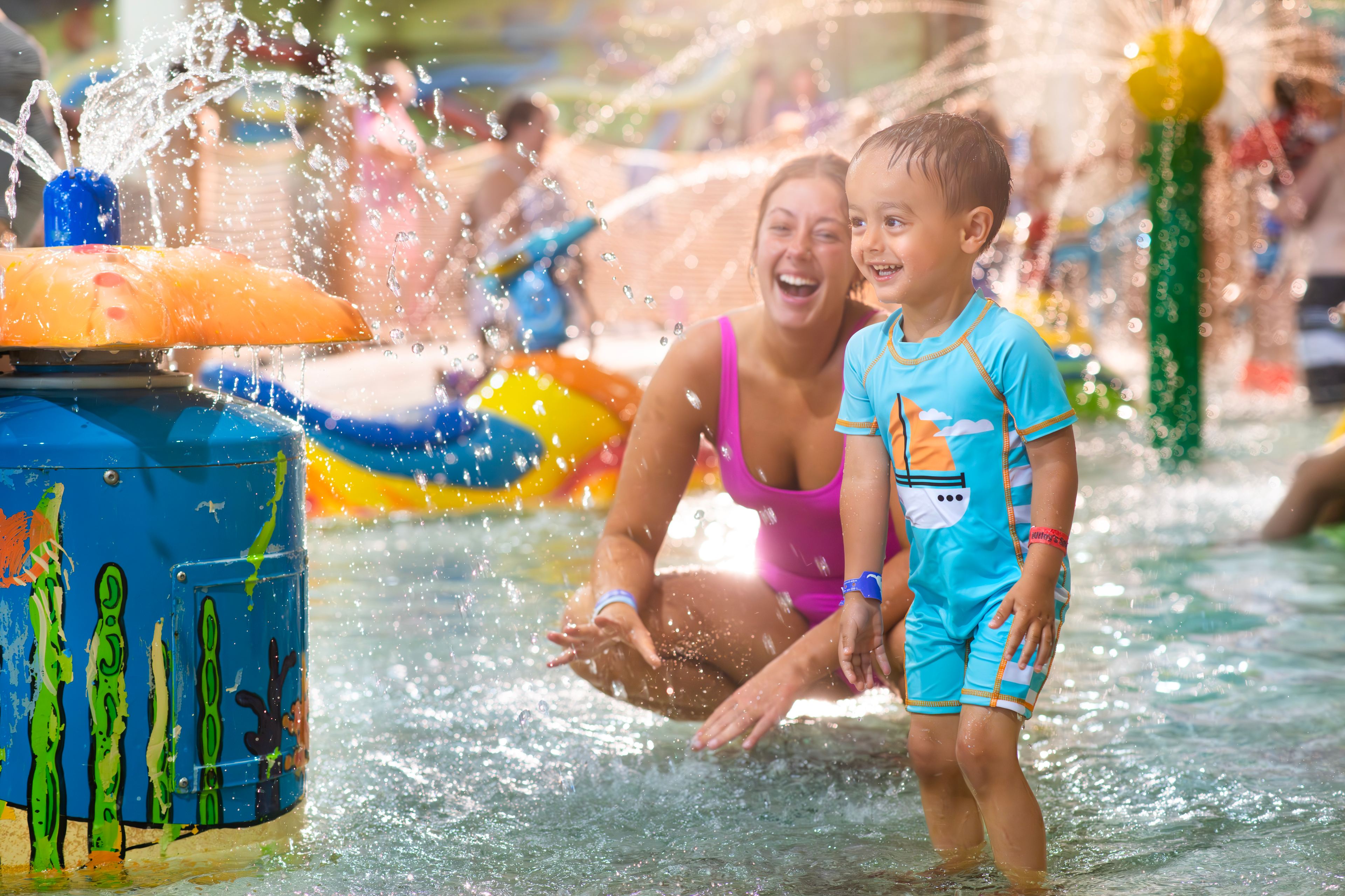 Adult and child laugh as water splashes down on them.
