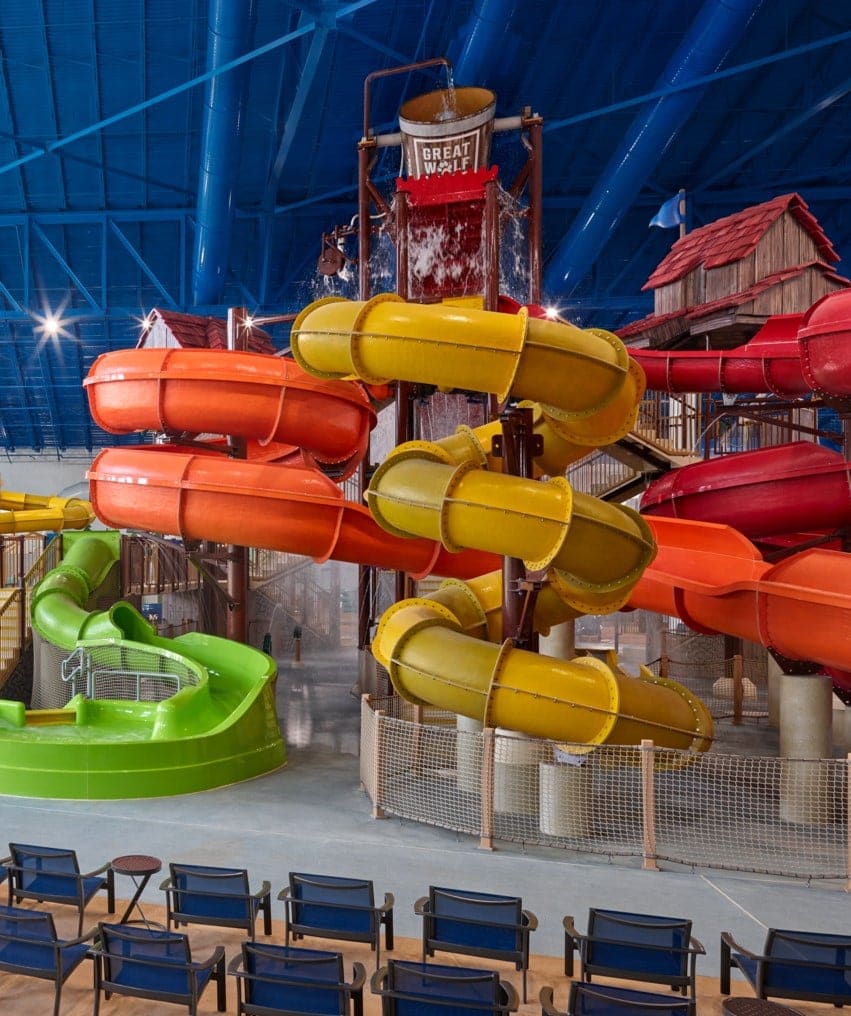 Indoor water park with colorful slides, splash bucket, and seating area under a blue ceiling.