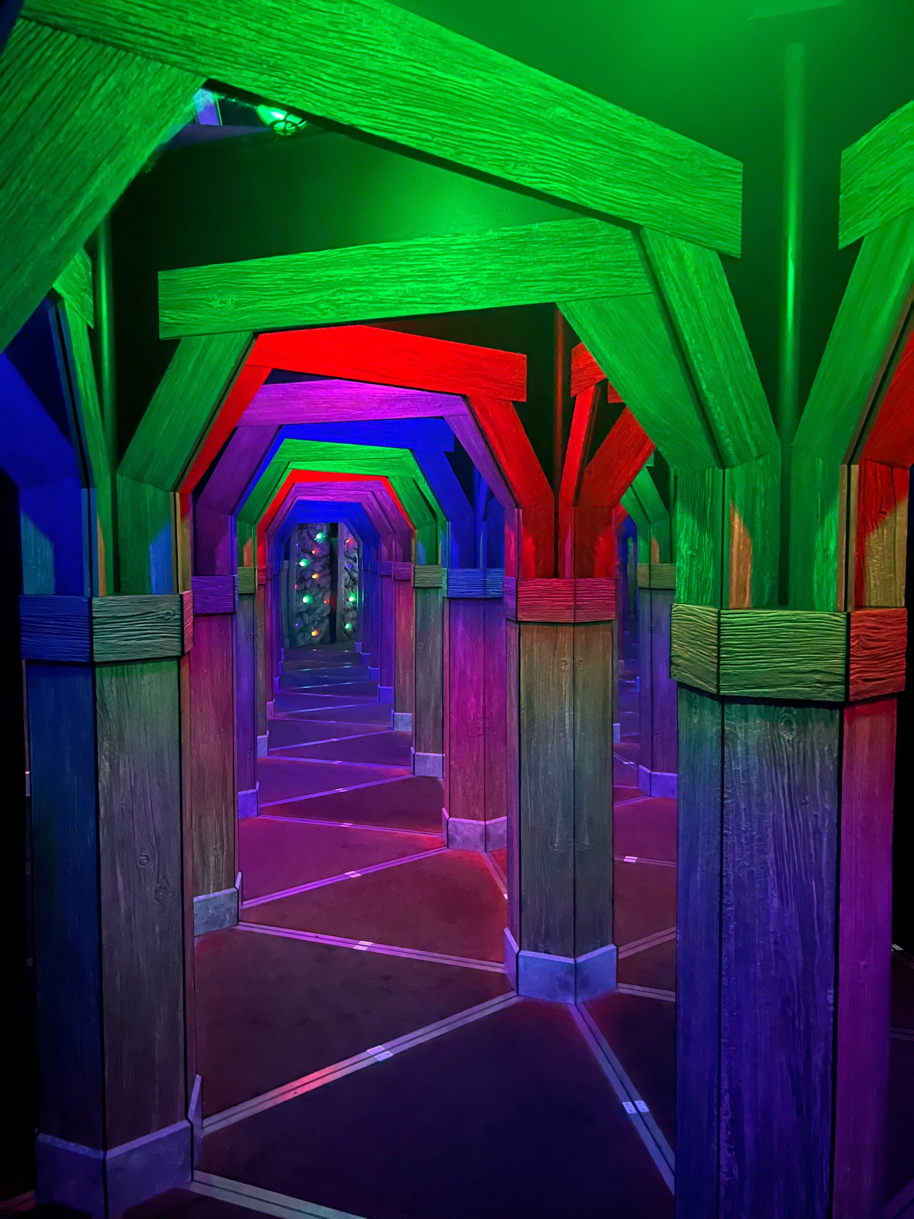Moonstone Mine Mirror Maze at Great Wolf Lodge, with mirrored wooden mine-shaft arches glowing green, red, blue and purple stretching down a long corridor.